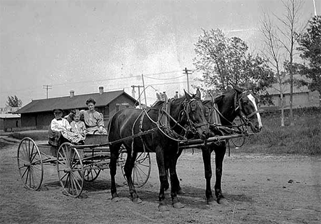 Woman and children in wagon in front of Forest Lake Railroad Station, Forest Lake Minnesota, 1906