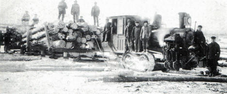 Photograph shows early logging operation of a steam hauler pulling a load of logs.