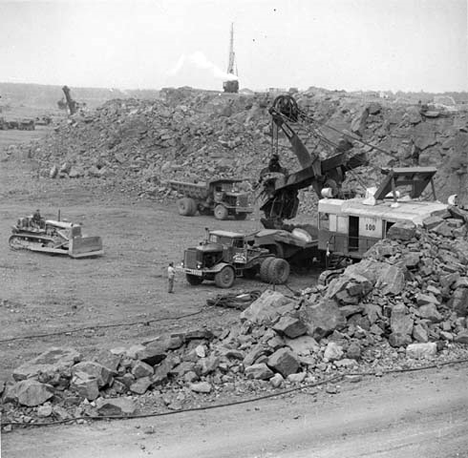 Taconite is blasted loose, then loaded by huge electric powered shovels into forty-five ton side dump trucks, Babbitt Minnesota, 1960