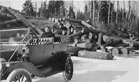 Man and woman in car examining the logs piled on the shore of the Big Fork River, Big Falls Minnesota, 1919